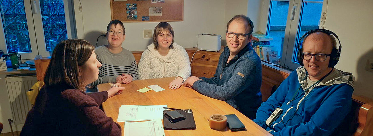 Fünf Personen sitzen gemeinsam am Tisch bei einem Besprechungstreffen