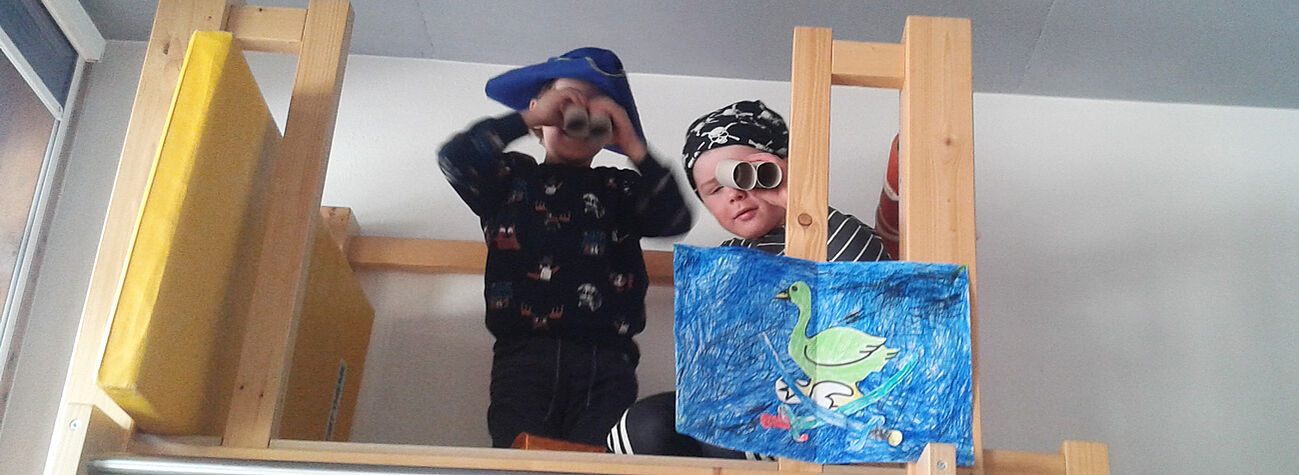 Zwei Kinder spielen verkleidet als Piraten auf einem Holzgerüst
